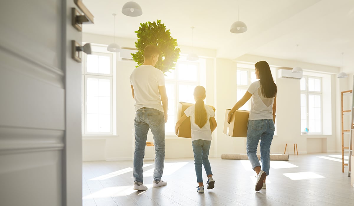Mom Dad and Daughter carrying boxes into empty home with sun glaring through windows