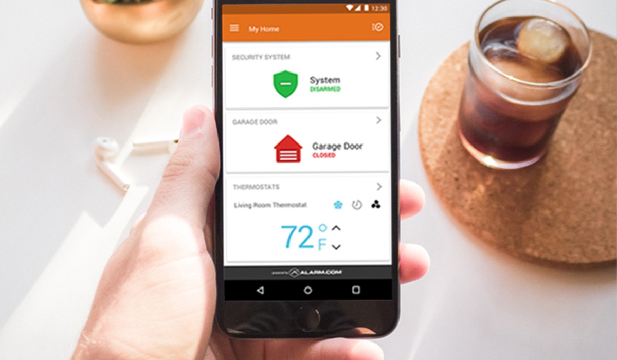 Hand holding phone showing Alarm.com application with security and temperature information