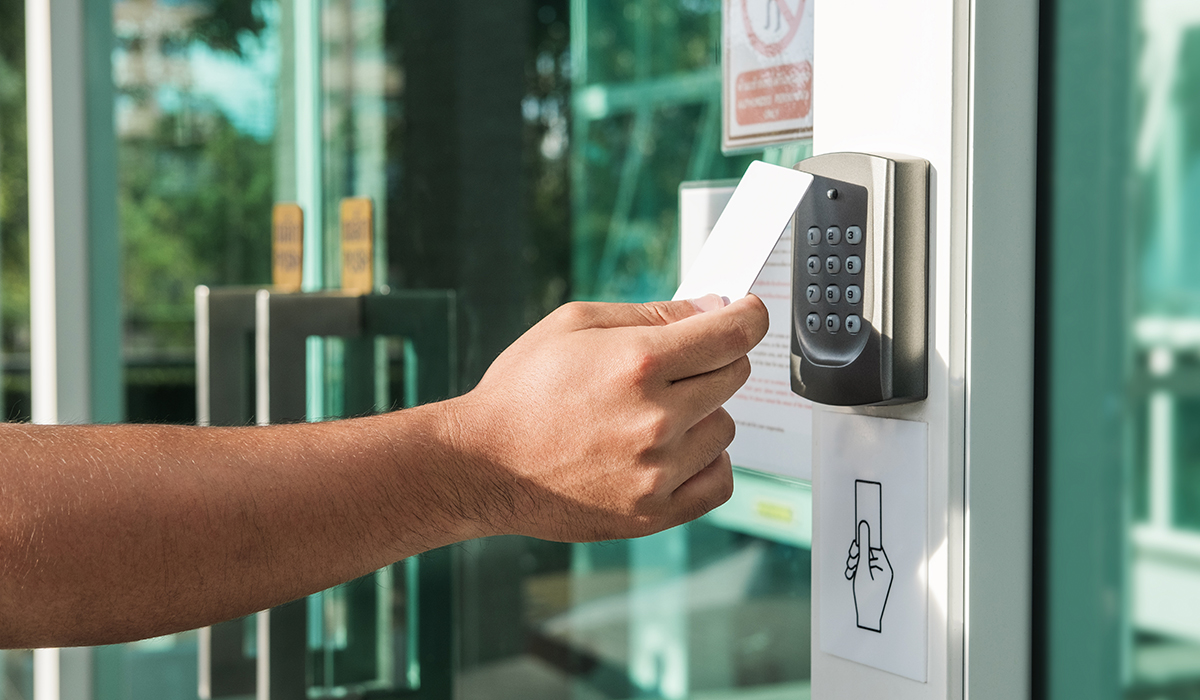 Arm holding out keycard in front of access control reader on sunny day