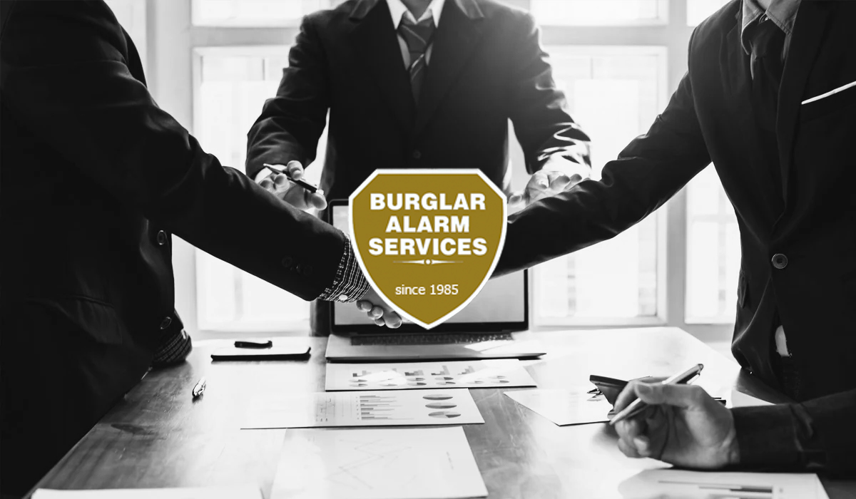 Black and white image of a business deal handshake with Burglar Alarm Services logo over top