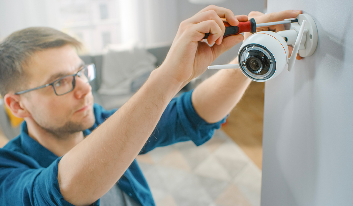 Guy with glasses and blue shirt using screwdriver to install wifi camera in brightly lit home