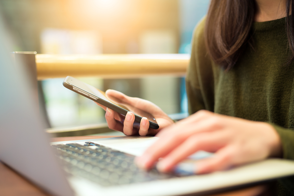 Woman connecting cell phone and laptop computer